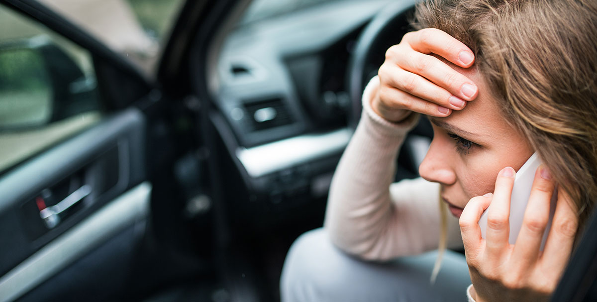 A woman with her hand on her head and on her cellphone after getting into a car accident Gibbons & Gibbons