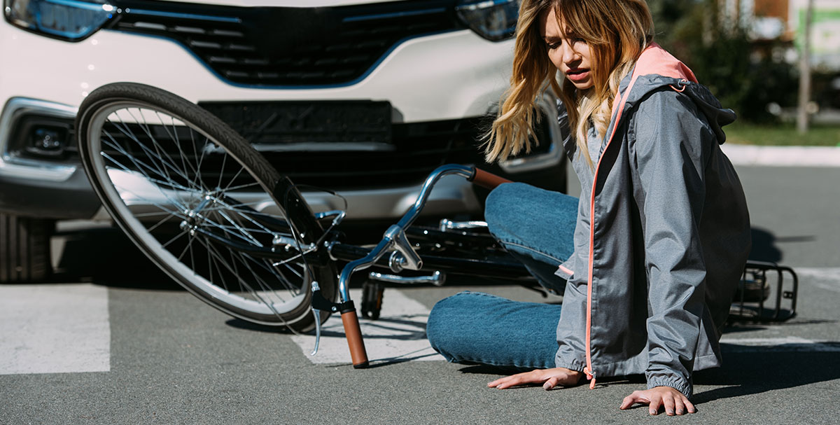 A woman hurt and on the ground with her bicycle after getting into a bicycle accident with a car