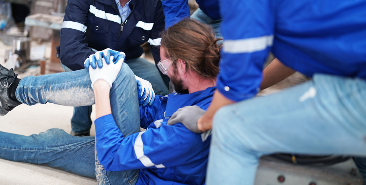 A working man hurt and holding his knee on the ground with co-workers surrounding him